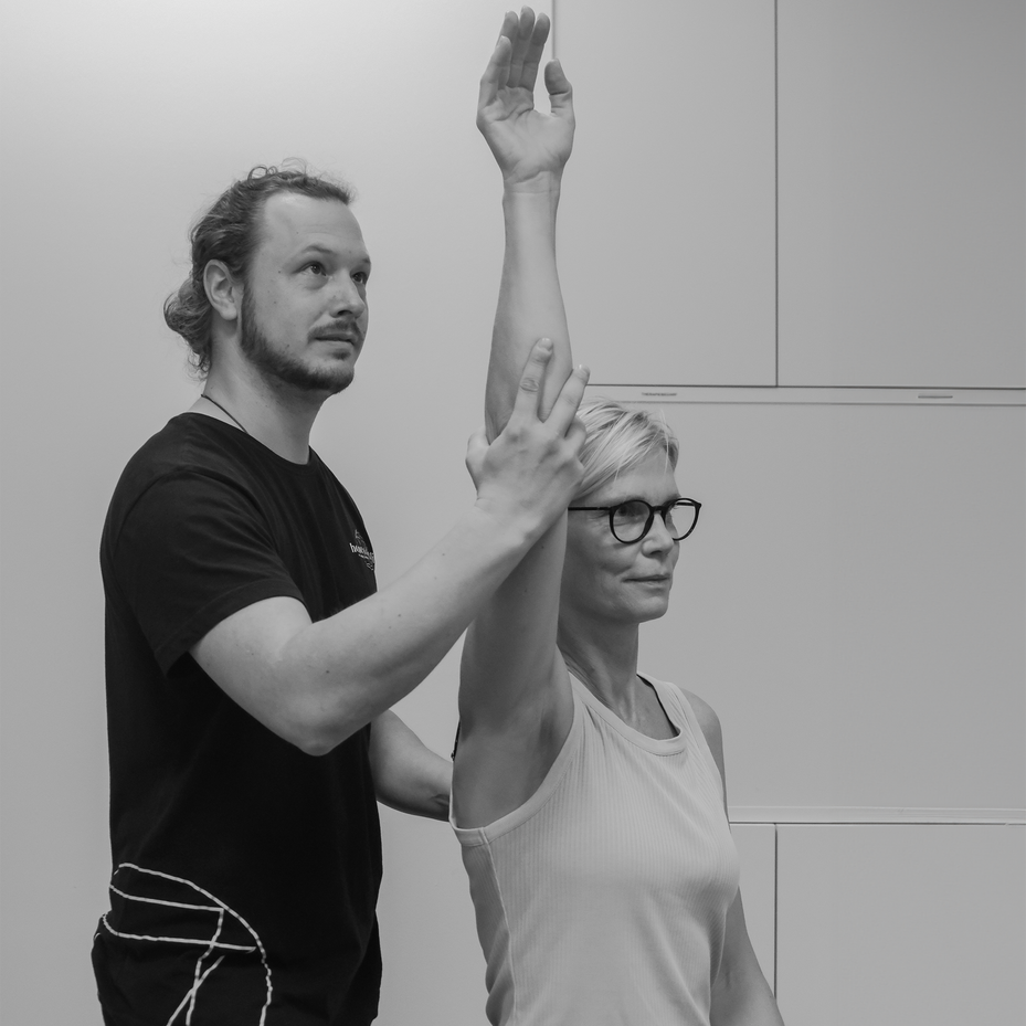 Frau bei Atemübungen neben Physiotherapeut, eine Hand in die Höhe gehalten