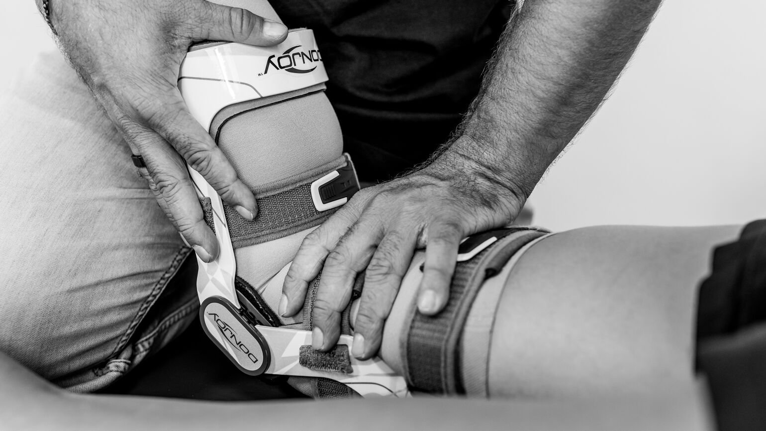 Therapeut führt in Bauchlage eine passive Mobilisation des Knies mit Orthese durch.