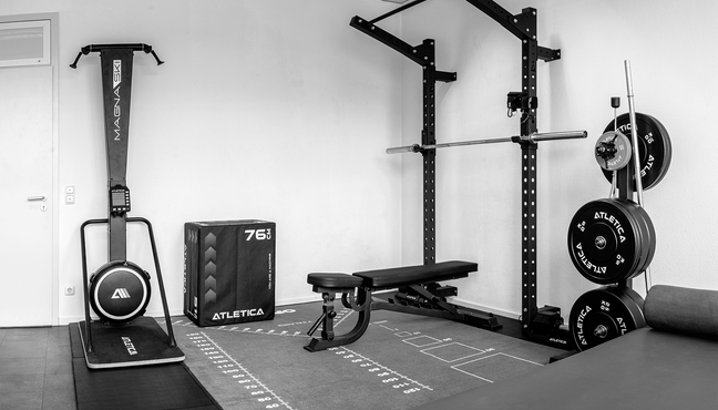 Trainingsraum mit Hantelbank, Kraftstation, Gewichtsscheiben und Fitnessgeräten.